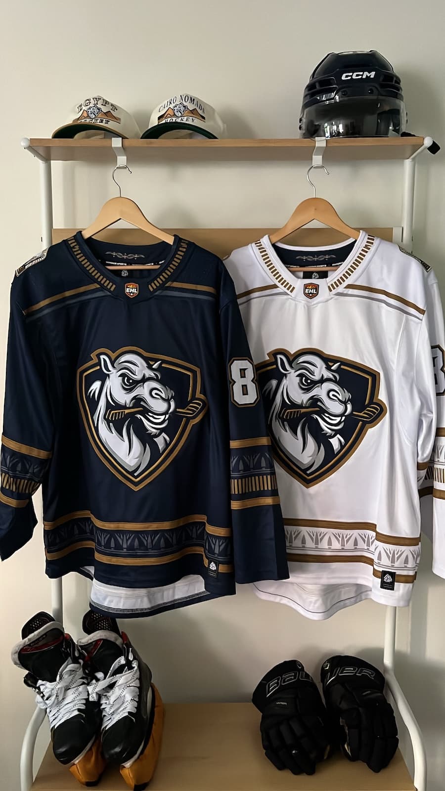 EHL home and away jerseys on a rack — navy and white sweaters with the club crest, above skates and gloves